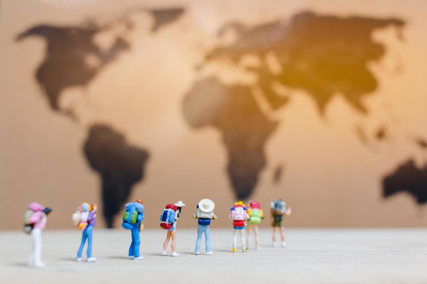 Miniaturreisende, die auf einer Weltkarte spazieren gehen, reisen und das Weltkonzept erkunden foto