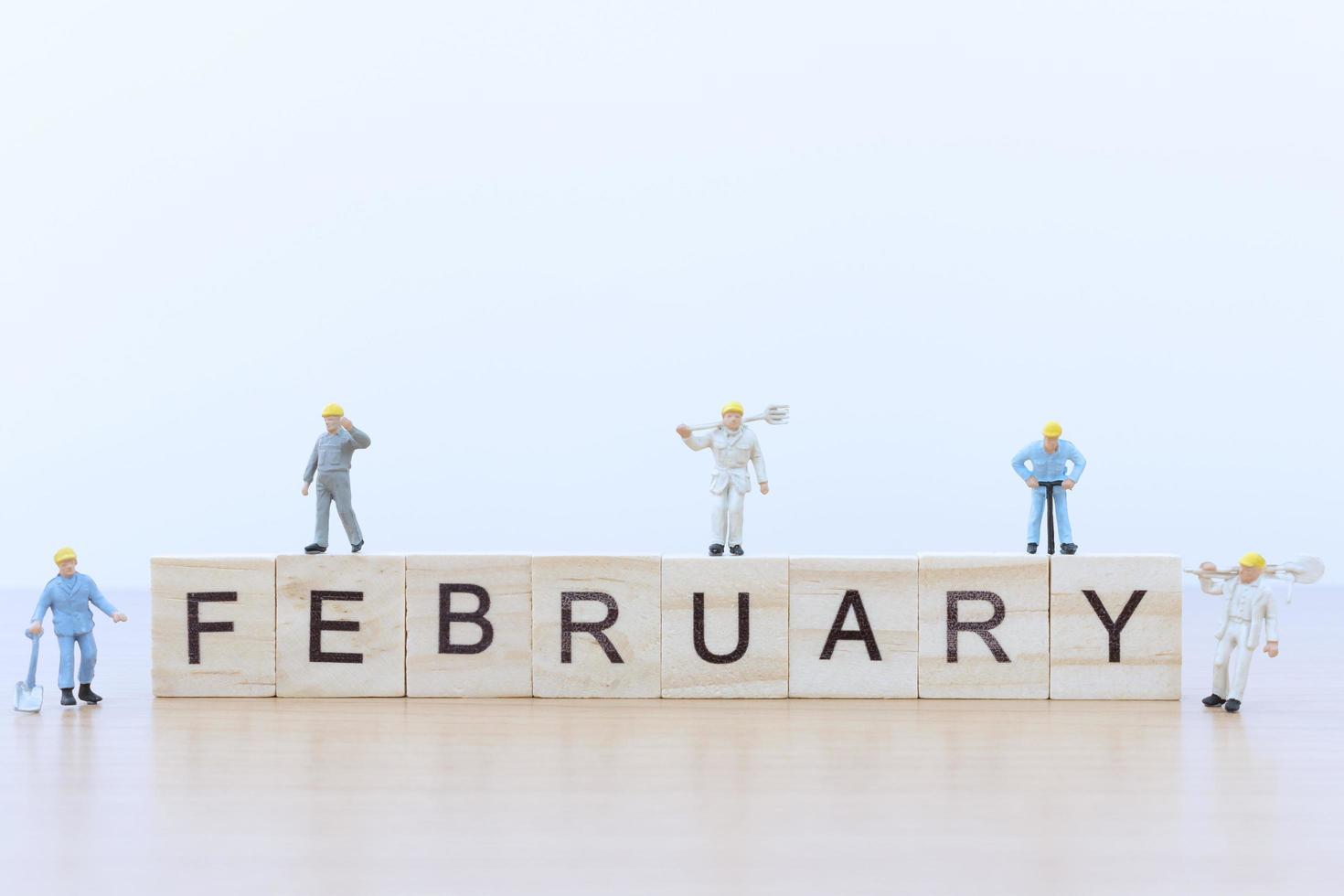 Miniaturmenschen, die an Holzklötzen mit dem Wort Februar auf einem Holzboden arbeiten foto