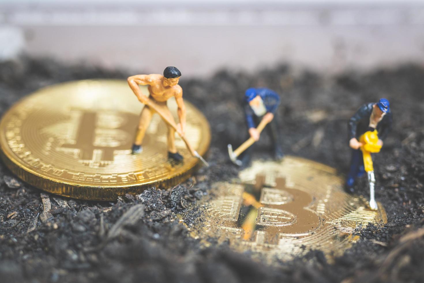 Miniaturarbeiter graben den Boden, um glänzende Bitcoin-Kryptowährung aufzudecken, erfolgreiches Arbeitskonzept foto