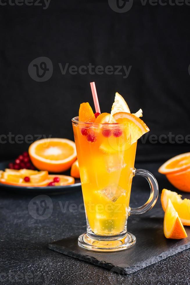 Orange Cranberry sprudelnd Cocktail im ein Glas und Früchte Nächster zu es auf ein dunkel Hintergrund. hausgemacht Mocktail. Vertikale Aussicht foto