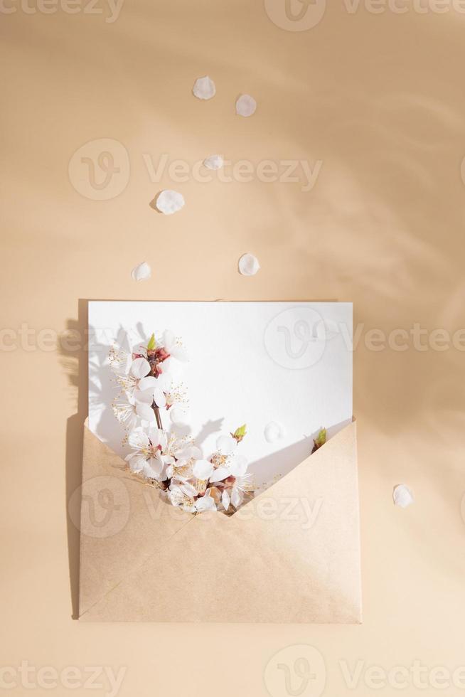 ein Briefumschlag mit zart Kirsche blühen Blütenblätter auf ein Beige Hintergrund. Frühling Vertikale spotten oben foto