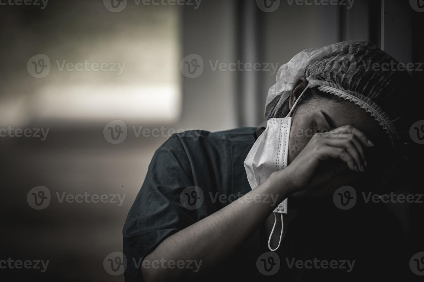 müde depressive asiatische krankenschwester trägt gesichtsmaske blaue uniform sitzt auf dem krankenhausboden, junge ärztin gestresst von harter arbeit foto