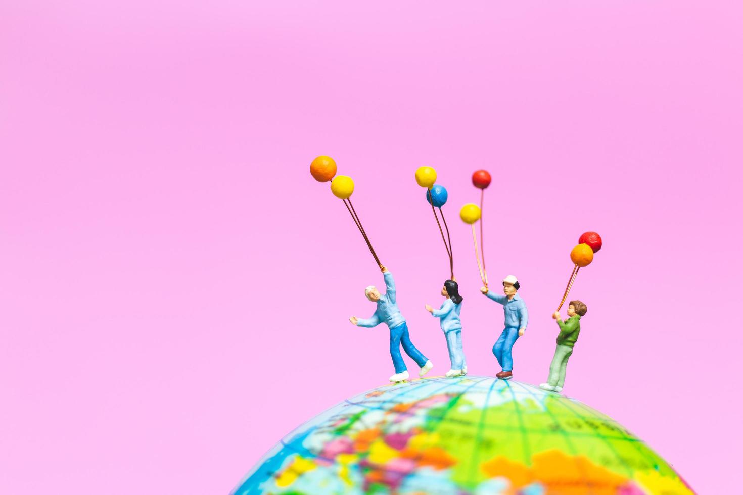 Miniaturfamilie, die Luftballons auf einem Globus mit einem rosa Hintergrund hält foto