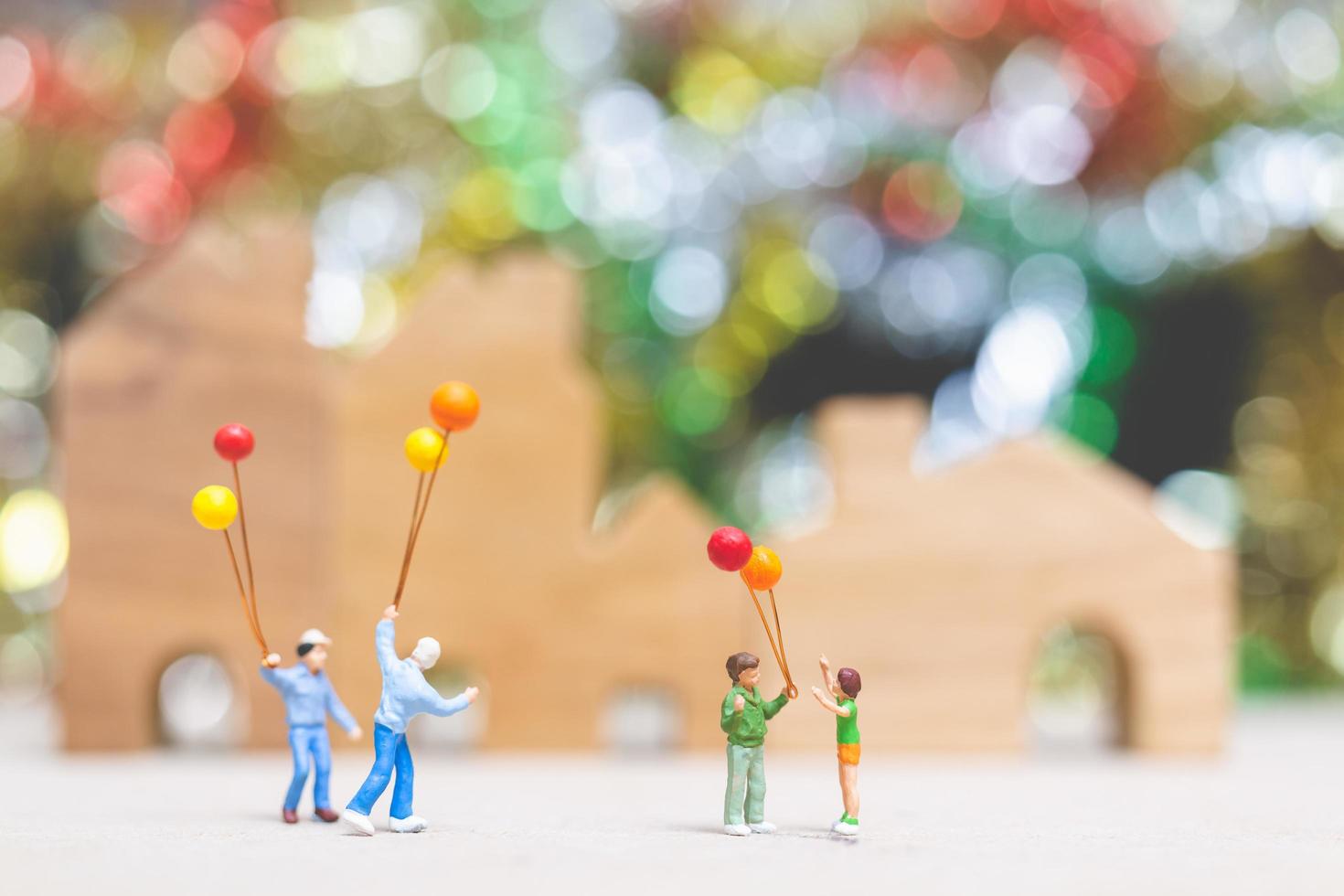 Miniaturleute, die Luftballons in einem Park mit einem bunten Bokehhintergrund, glücklichen Familienbeziehungen und sorglosem Freizeitkonzept halten foto