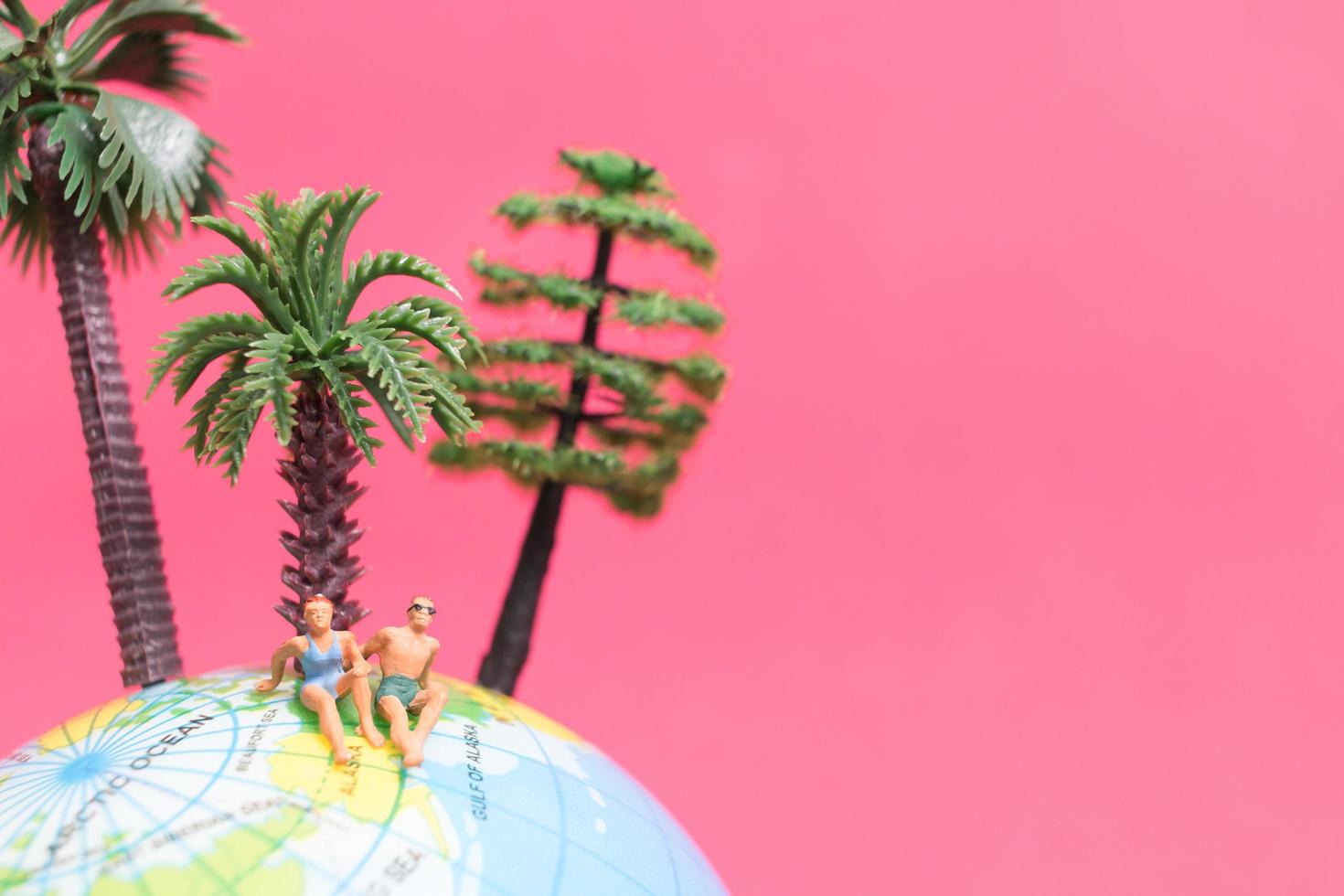 Miniaturmenschen, die Badeanzüge tragen, die auf einem Globus mit einem rosa Hintergrund, Flitterwochenkonzept entspannen foto