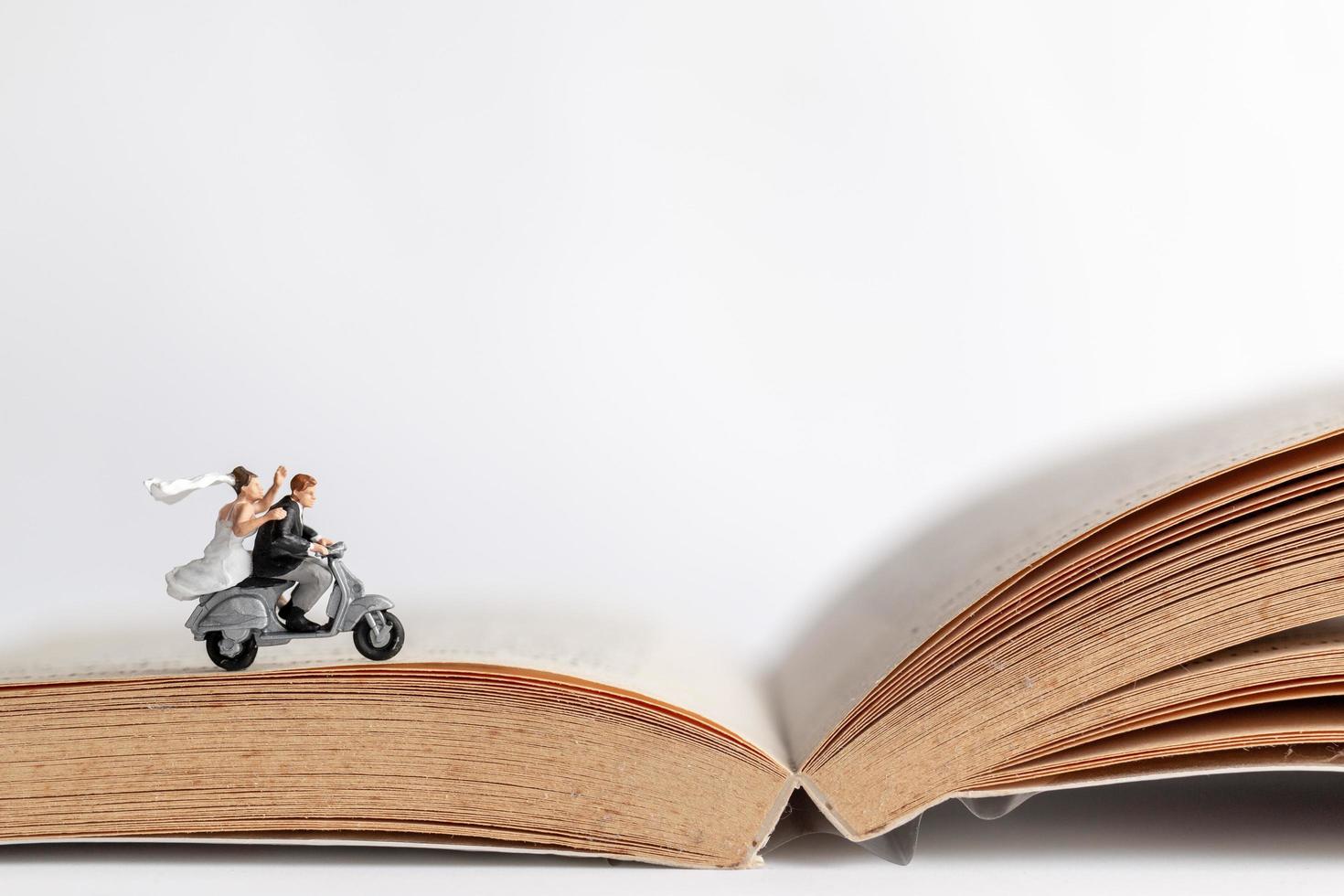Miniaturpaar, das ein Motorrad auf einem alten Buch fährt, Valentinstagkonzept foto