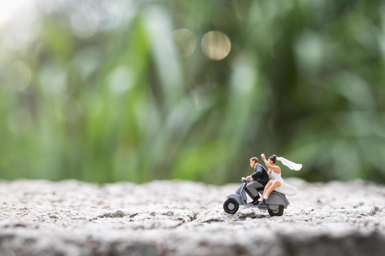 Miniaturpaar, das ein Motorrad auf einem unscharfen Naturhintergrund reitet foto