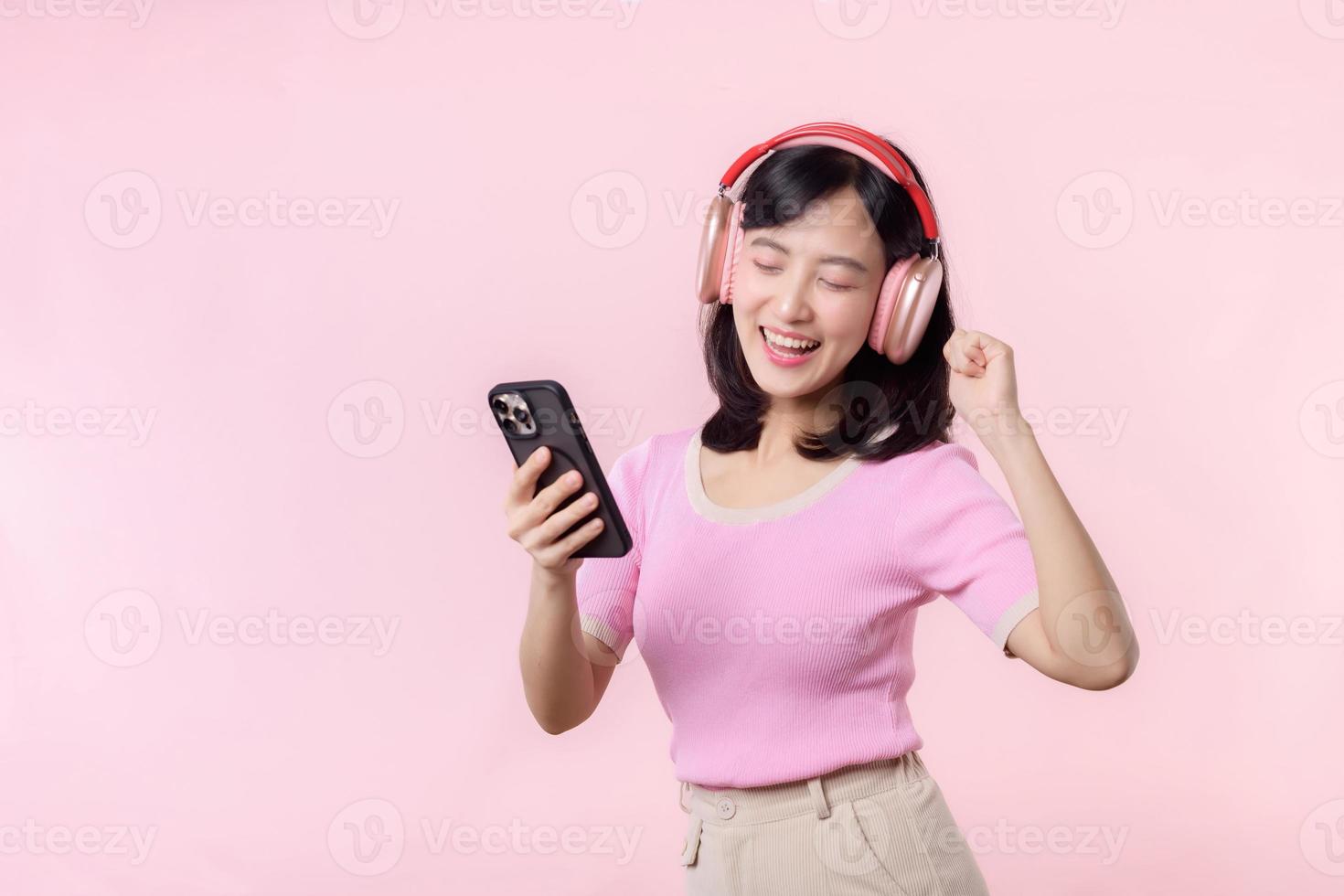 Porträt heiter jung asiatisch Frau genießen Hören Audio- durch Smartphone Musik- Anwendung gegen Rosa. glücklich lächelnd weiblich Person mit Kopfhörer. Klang, Freizeit, Lebensstil, Technologie Konzept foto