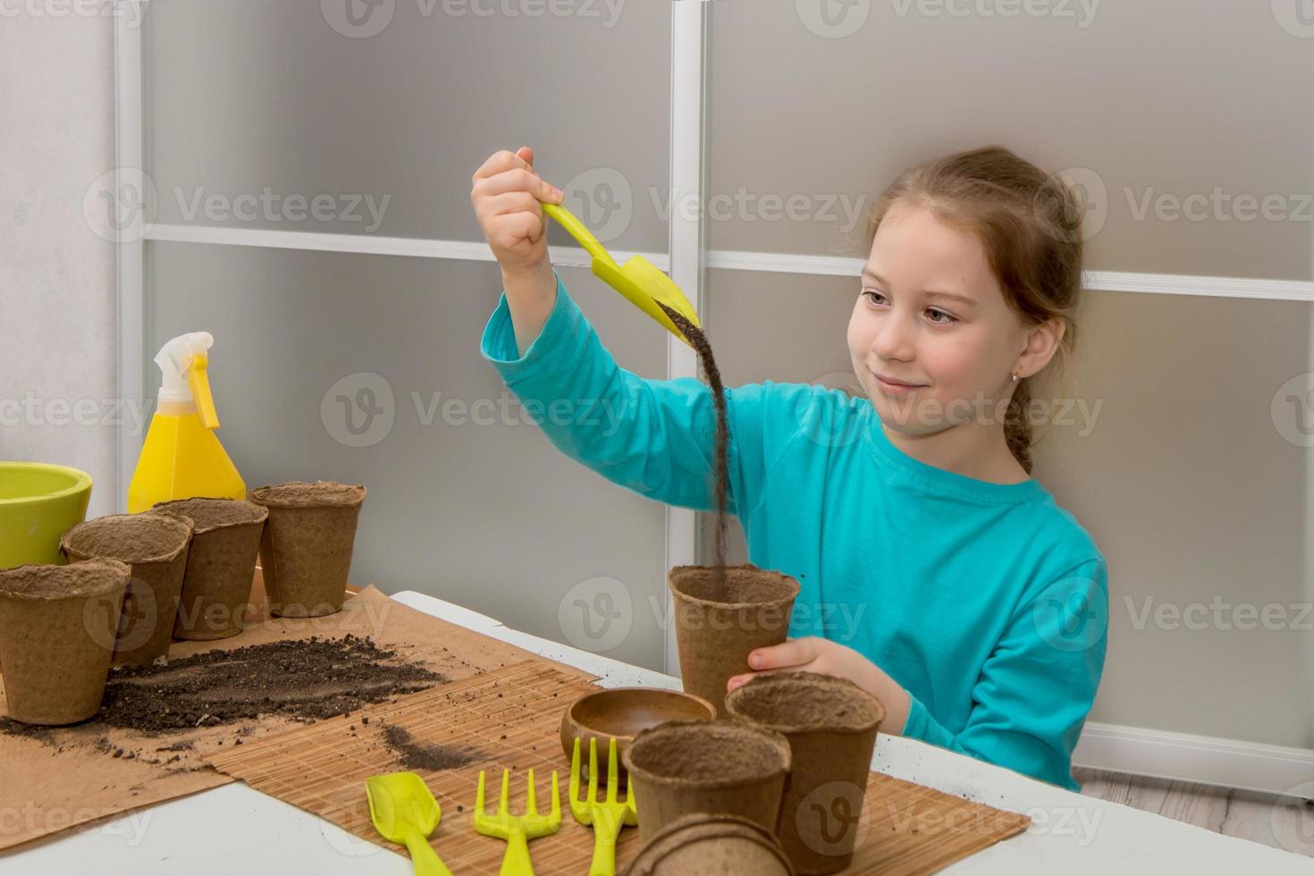 süß wenig Mädchen gießt Sand von ein Schaufel in ein Torf Topf im Vorbereitung zum Pflanzen Sämlinge foto