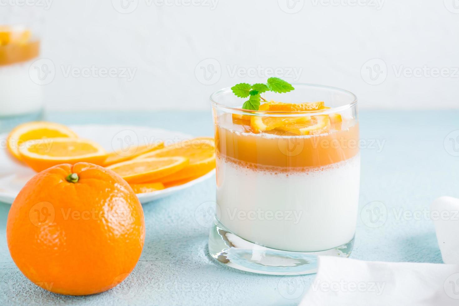 hausgemacht Panna Cotta mit Orange und Minze Blatt im ein Glas und ein ganze Orange auf ein Licht Tisch. Süss Italienisch Dessert foto