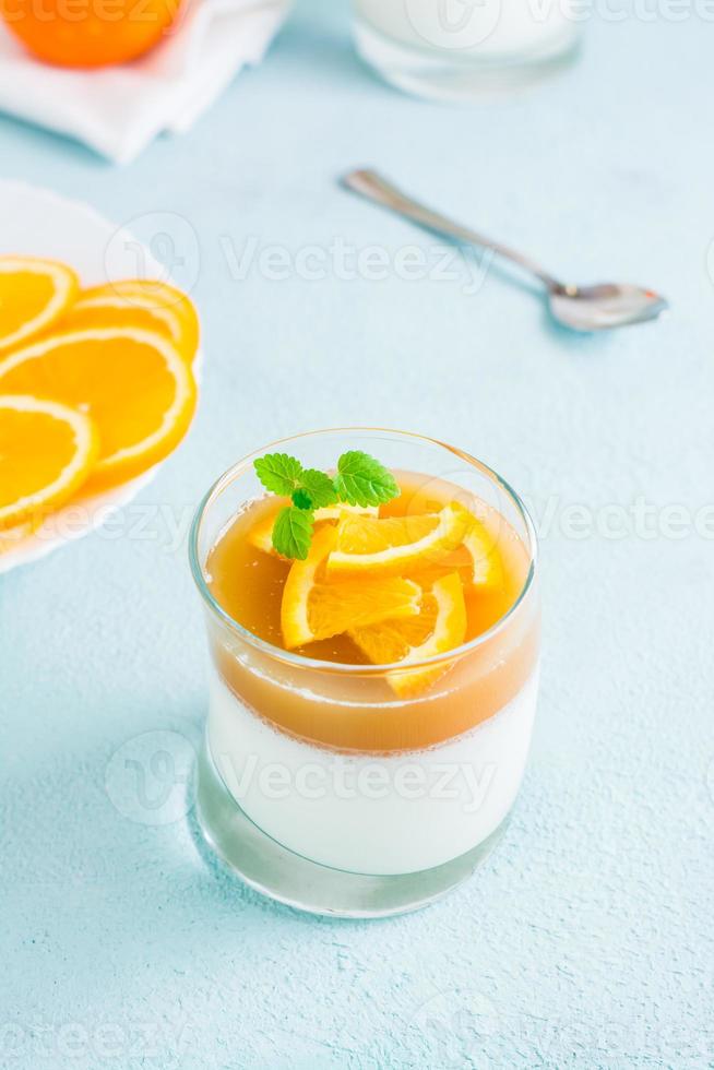 hausgemacht Panna Cotta mit Orange und Minze Blatt im ein Glas auf ein Licht Tisch. Süss Italienisch Nachtisch. Vertikale Sicht. Nahansicht foto