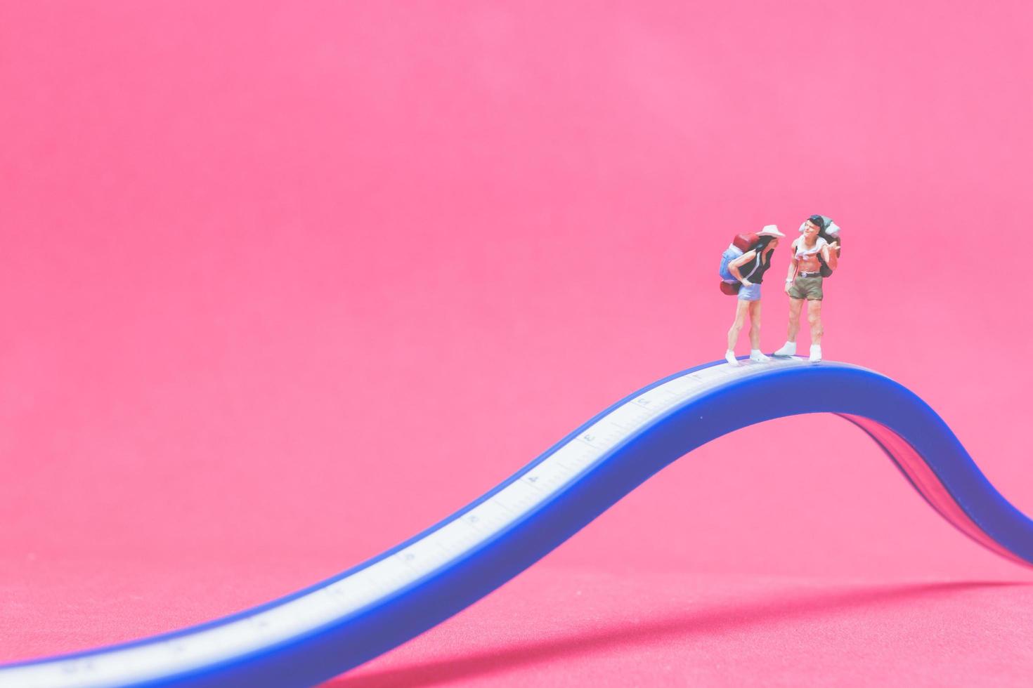 Miniaturpaar von Reisenden auf einer Brücke mit einem rosa Hintergrund foto