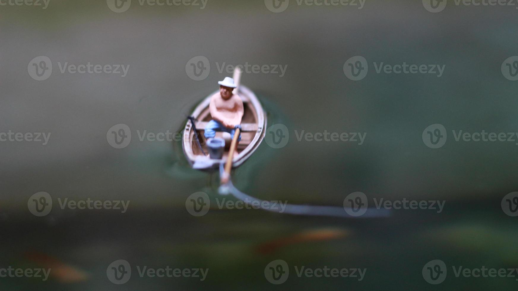 Miniatur Zahl von ein Fischer Angeln auf ein See im ein klein Boot. foto