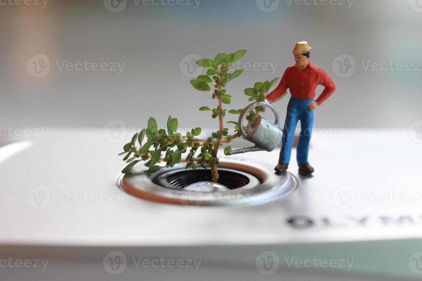ein Miniatur Zahl von ein Farmer Bewässerung ein eingetopft Pflanze im das bilden von ein analog Kamera Linse. foto