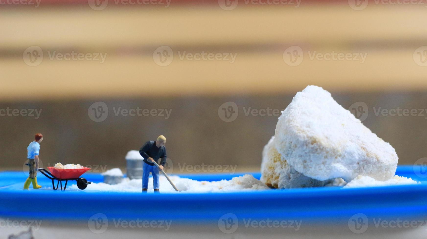 ein Miniatur Zahl von ein Arbeiter Aufräumen ein Erdnuss Kuchen bestreut mit pulverisiert Weiß Zucker. Konzept von Arbeitskräfte im das Essen Industrie. foto