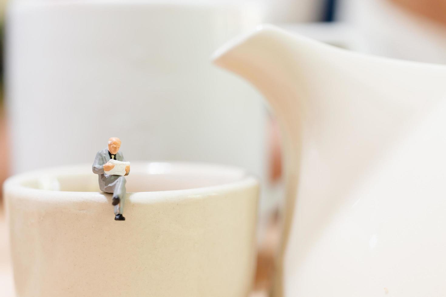 Miniaturgeschäftsmann, der auf einer Teetasse sitzt foto