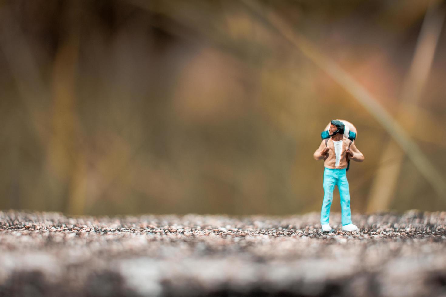 Miniatur-Rucksacktourist, der auf einem Betonboden mit einem Bokeh-Naturhintergrund steht foto