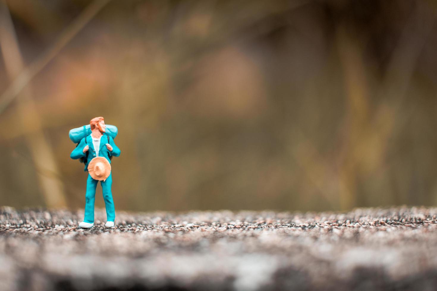 Miniatur-Rucksacktourist, der auf einem Betonboden mit einem Bokeh-Naturhintergrund steht foto