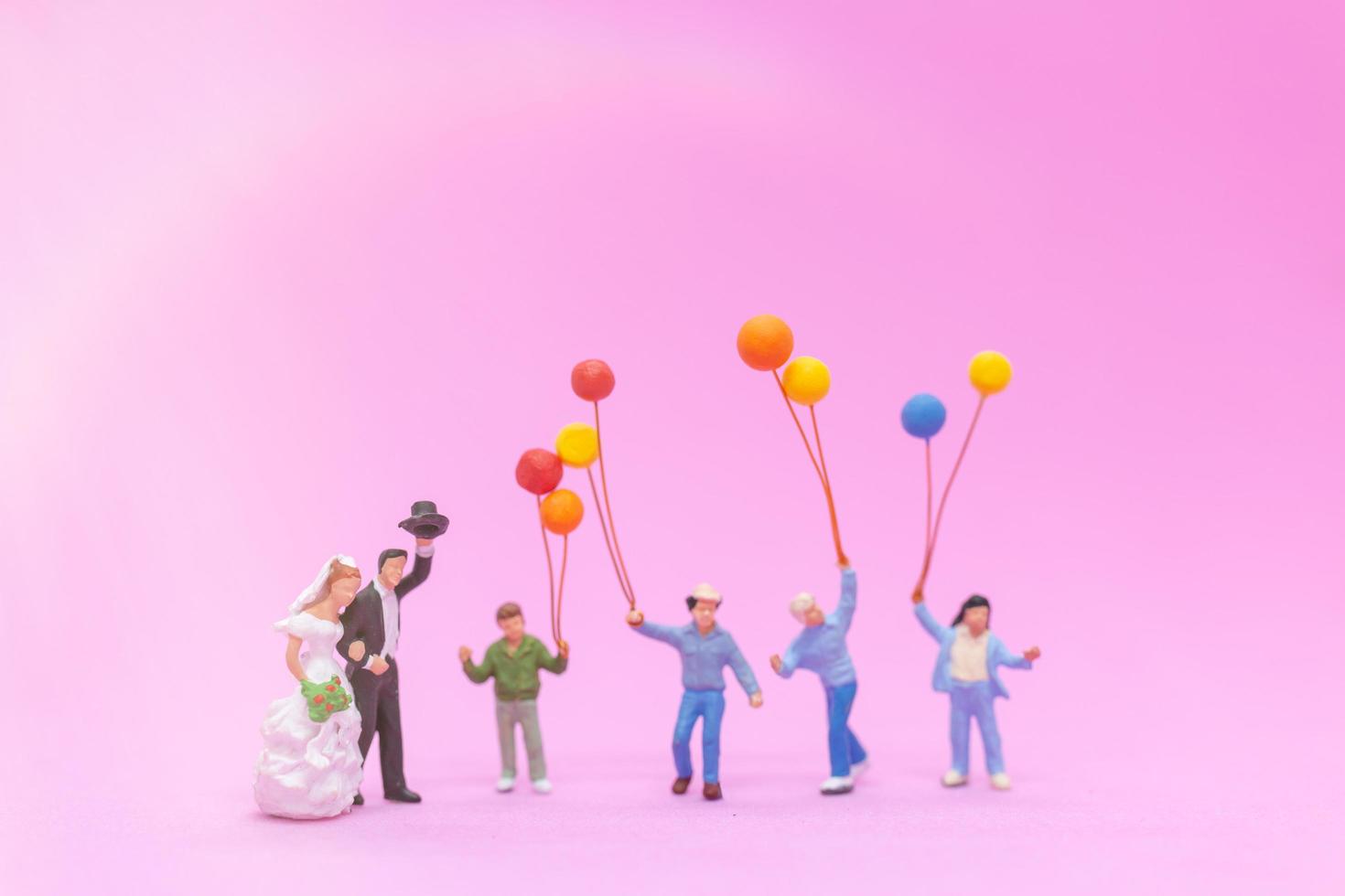 Miniaturpaar und Familie mit bunten Luftballons, die auf einem rosa Hintergrund feiern, Hochzeitskonzept foto