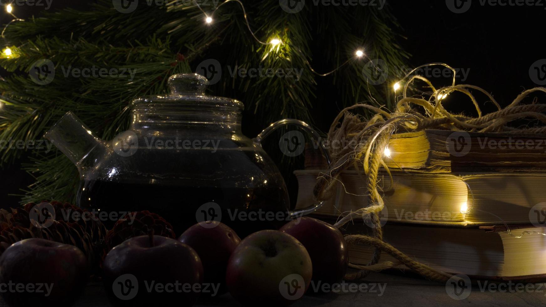 Glas Teekanne, alt Bücher, Kiefer Bäume und Äpfel. Girlande Beleuchtung. Nacht Bild. Weihnachten Stimmung. foto