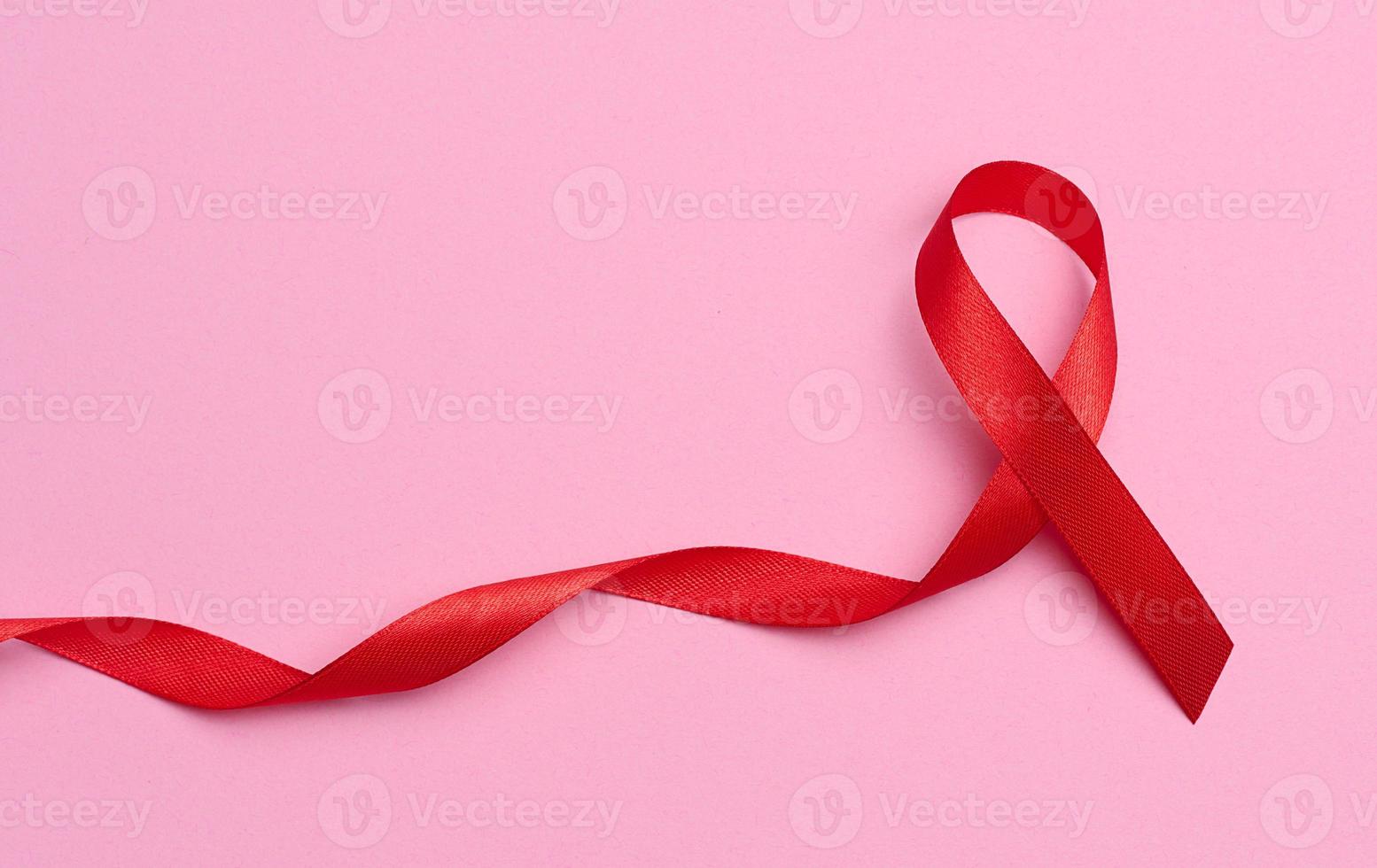 ein Seide rot Band im das bilden von ein Bogen auf ein Rosa Hintergrund, ein Symbol von das Kampf gegen AIDS und ein Zeichen von Solidarität und Unterstützung foto