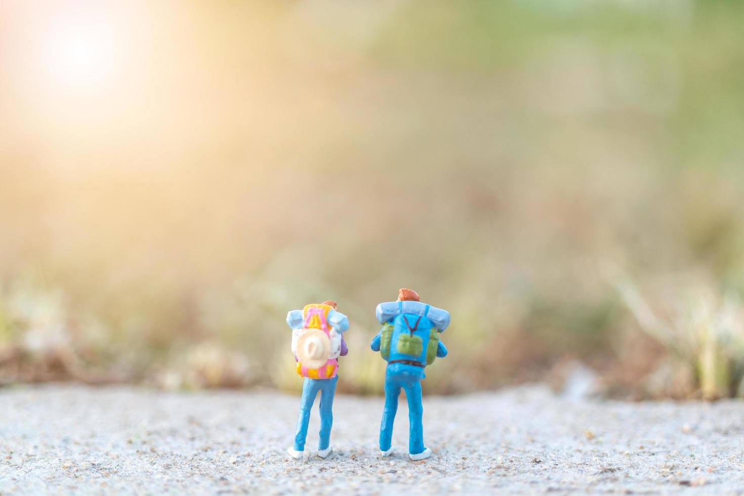 Miniaturreisende mit Rucksäcken, die auf einem Straßen-, Reise- und Abenteuerkonzept stehen foto