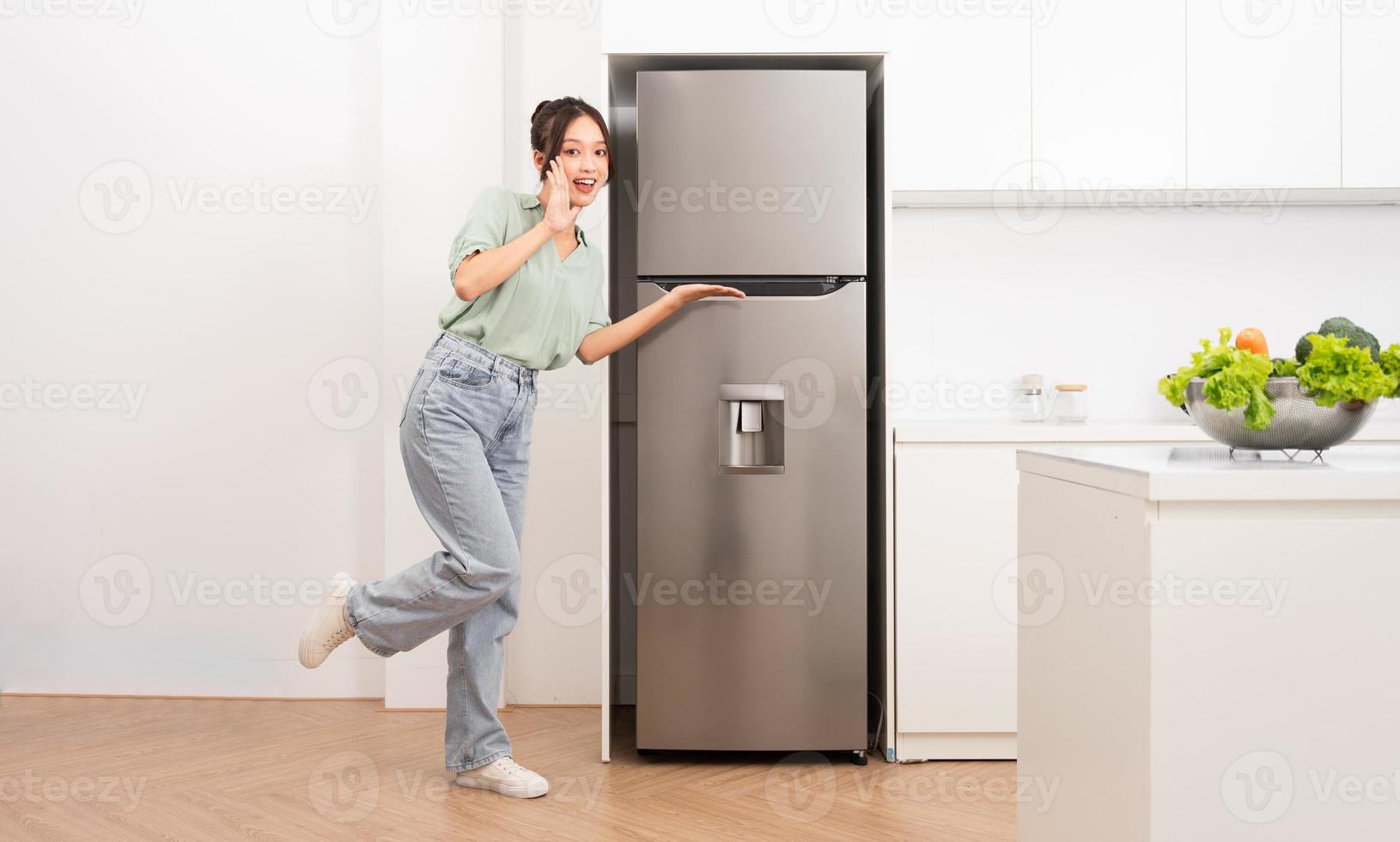 asiatisch Frau Stehen Nächster zu das Kühlschrank im das Küche foto