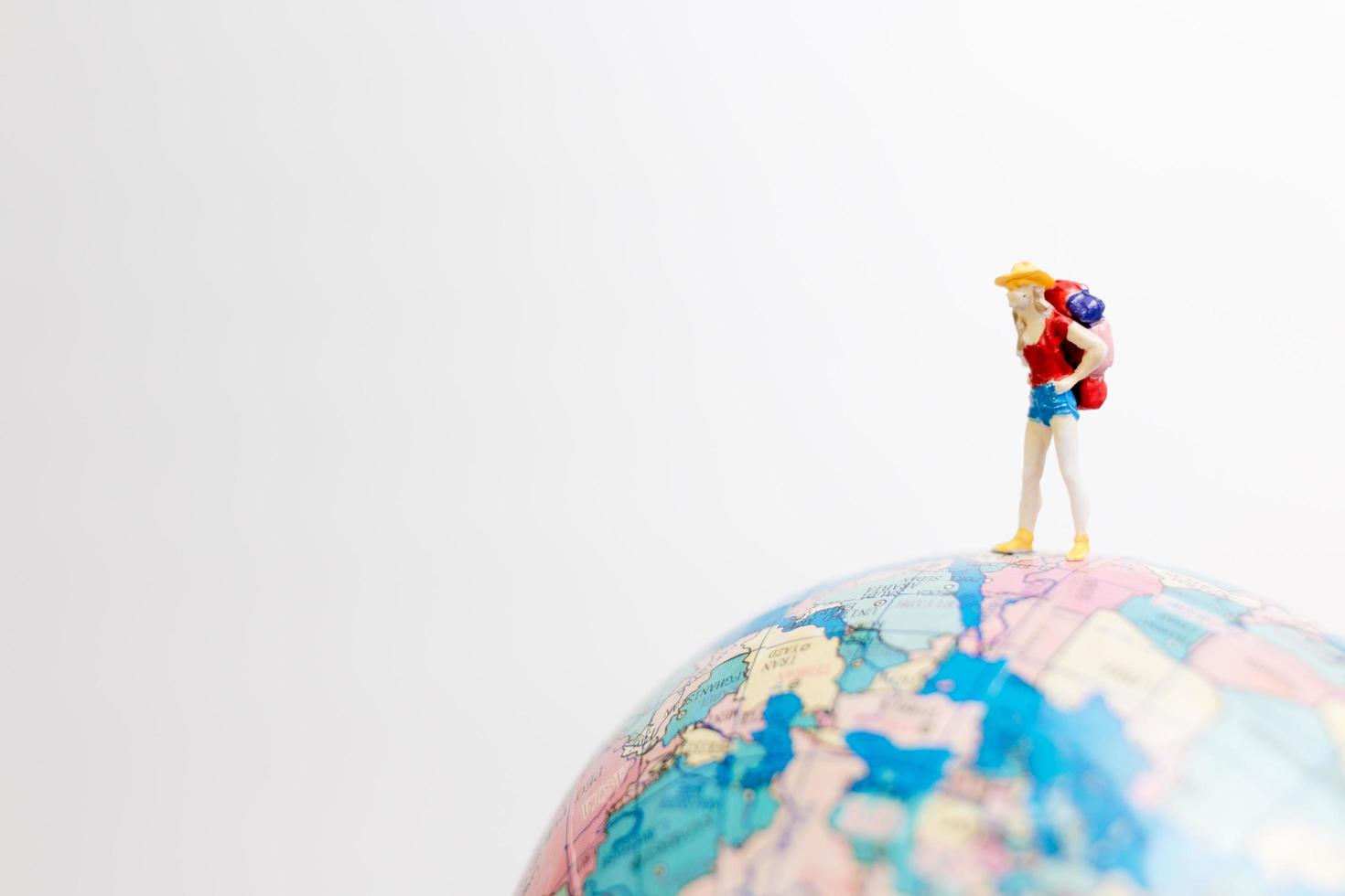Miniaturperson, die auf einem Globus mit einem weißen Hintergrund, Reisekonzept steht foto