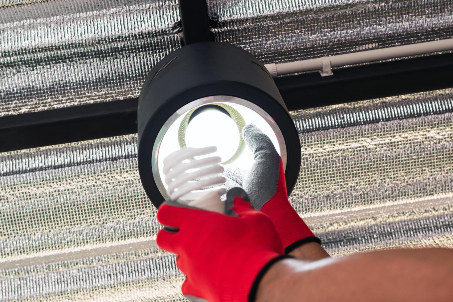 Paar Hände in roten Handschuhen, die eine Leuchtstofflampe durch eine LED-Lampe ersetzen foto