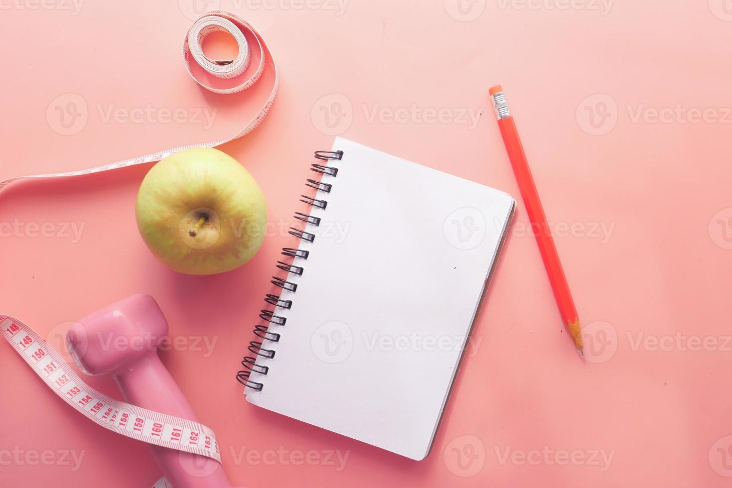 Fitnesskonzept mit Hantel, Apfel und Notizblock auf rosa Hintergrund foto
