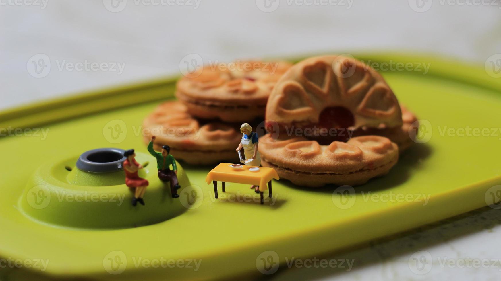 Miniatur zahlen von ein Paar reden auf ein Grün Essen Tabelle in der Nähe von ein Koch Kochen auf ein Hintergrund von ein Kuchen gefüllt mit Erdbeere Marmelade. Diskussion Konzept. foto
