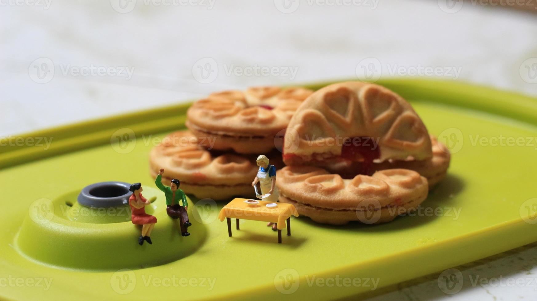 Miniatur zahlen von ein Paar reden auf ein Grün Essen Tabelle in der Nähe von ein Koch Kochen auf ein Hintergrund von ein Kuchen gefüllt mit Erdbeere Marmelade. Diskussion Konzept. foto