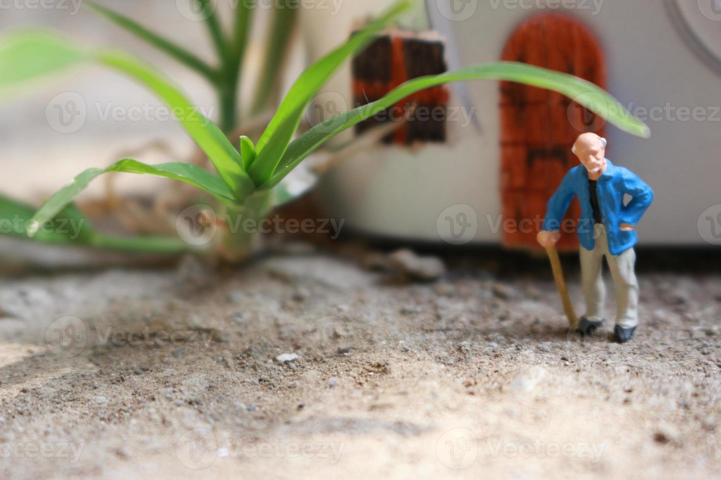 Miniatur Zahl von ein Großvater Wer ist warten im Vorderseite von das Haus. foto