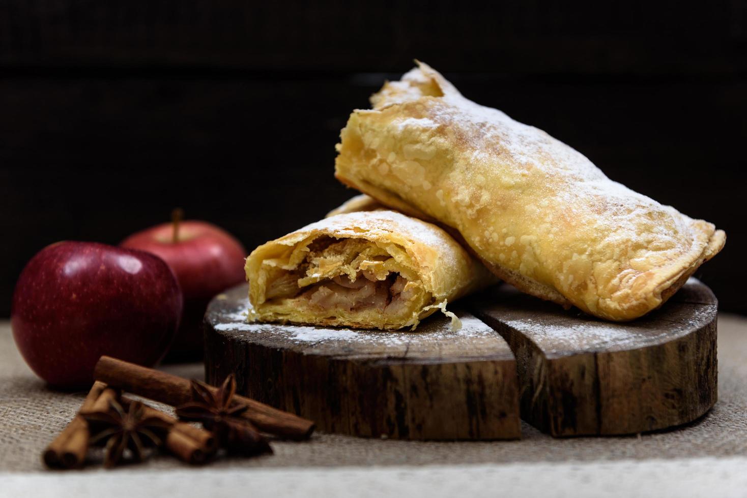 Apfelstrudel am hölzernen Ende eines Baumes mit Äpfeln, Zimt und Sternanis foto