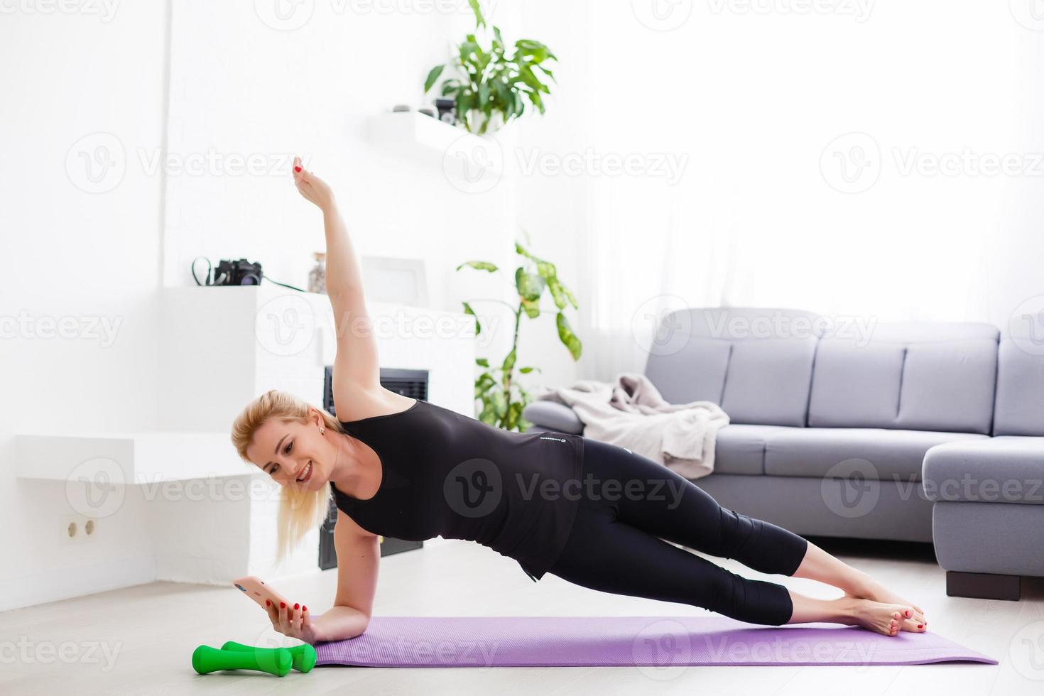 ein dünn europäisch Mädchen tun Dehnen Übungen beim Zuhause auf ein Yoga Matte, Strahlen von Licht scheinen von das Fenster. aufflackern. Quarantäne Sport. foto