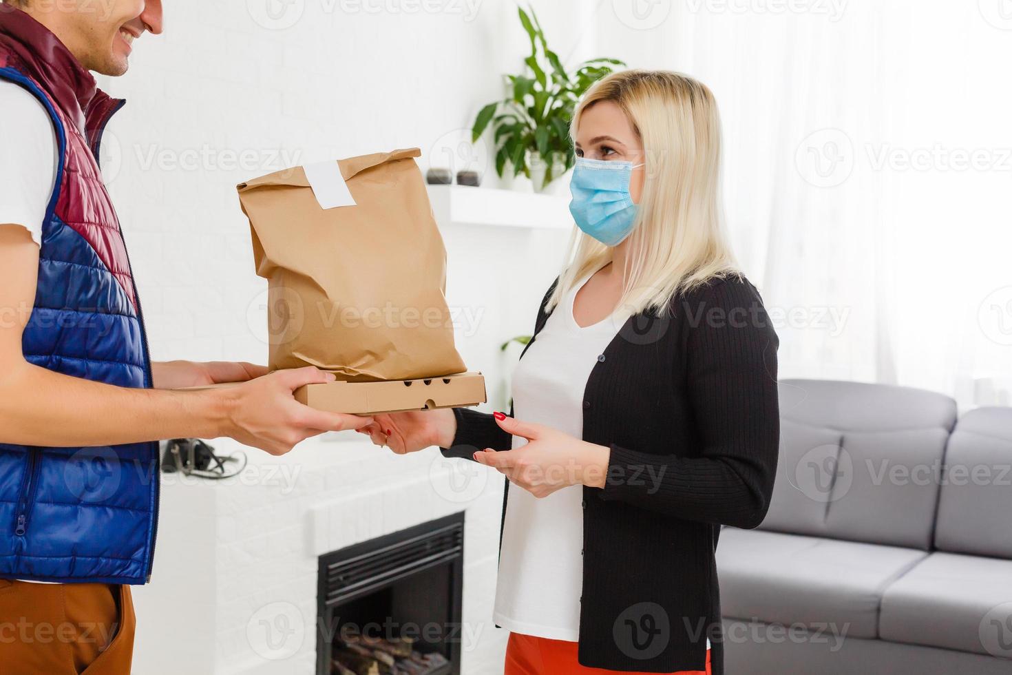 jung Frau tragen medizinisch Maske Empfang Paket von Lieferung Mann drinnen. Verhütung von Virus Verbreitung foto