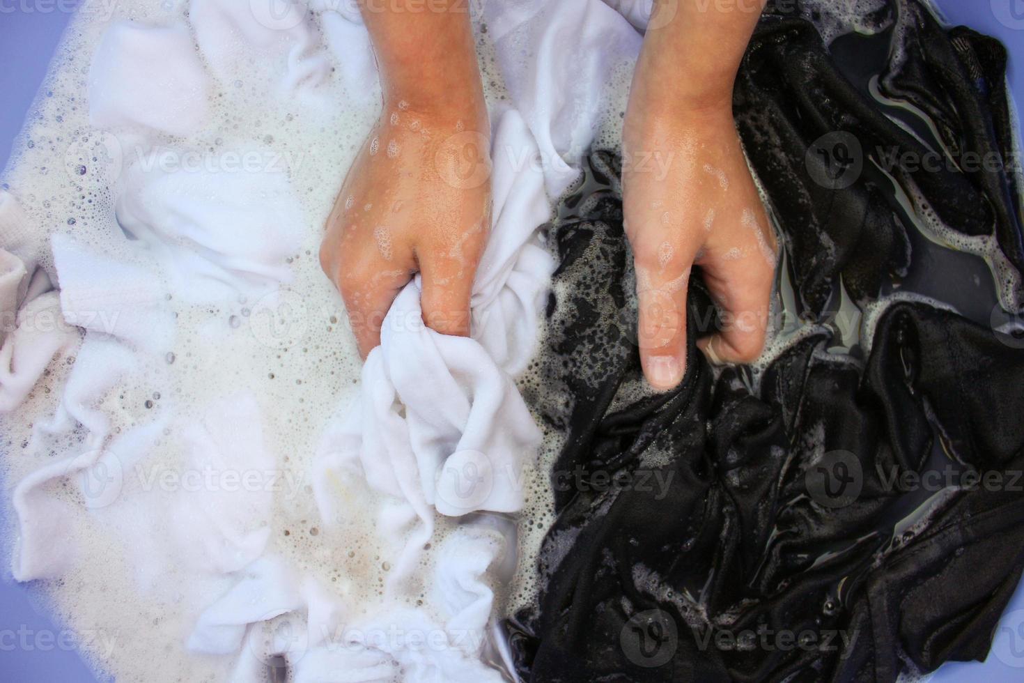 weiblich Hand waschen schwarz und Weiß Kleider im gleich Becken. foto