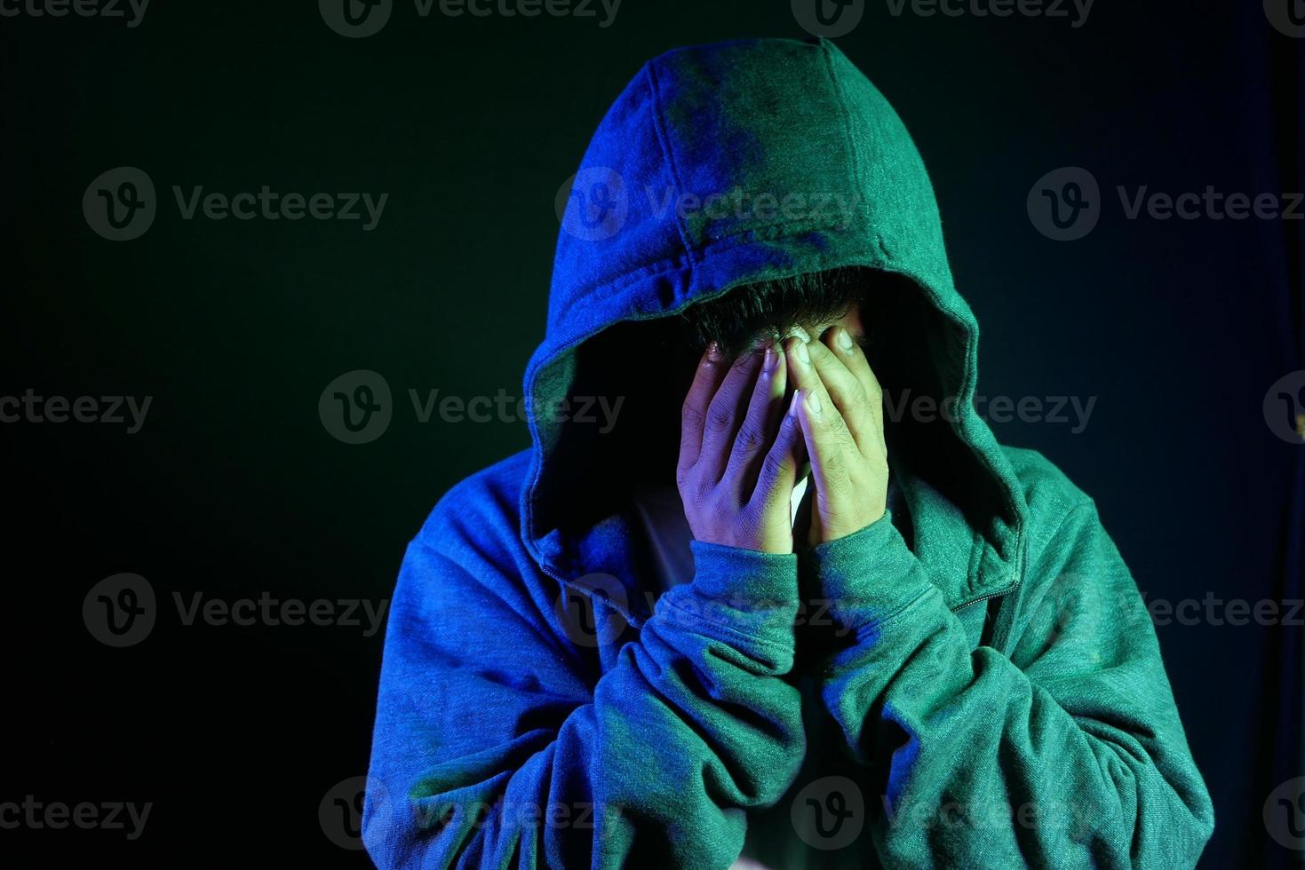 Mann in der Kapuze, die Gesicht mit Händen bedeckt foto