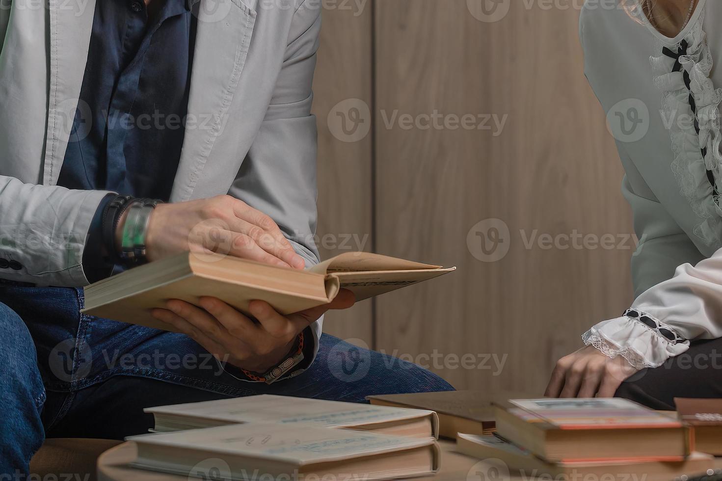 ein Mann und ein Frau sitzen beim ein Tabelle und aussehen durch Bücher zusammen, ein Lehrer und ein Schüler lesen lehrreich Literatur, bereiten zum ein Vorlesung, schreiben ein These foto