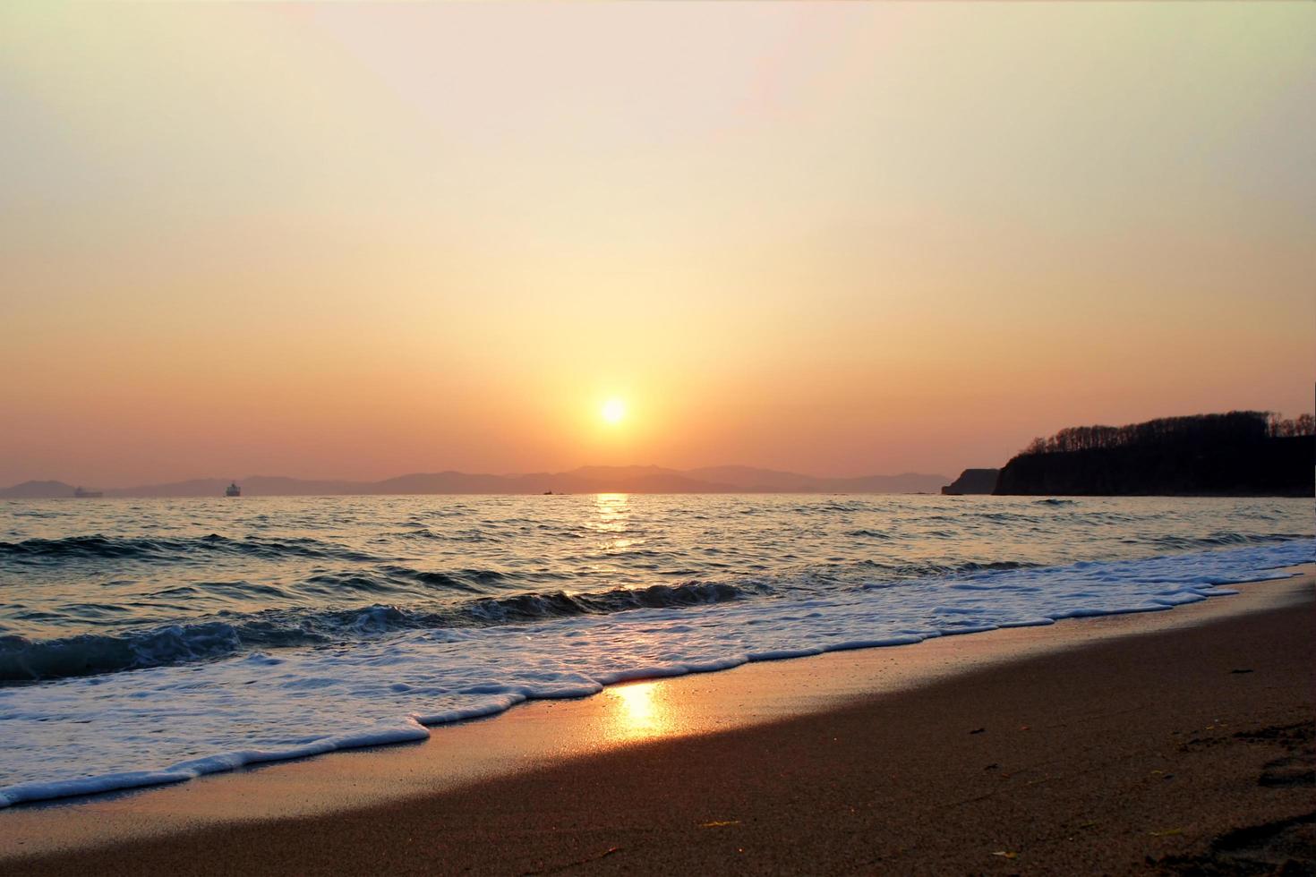 Wellen, die auf einem Strand mit orange bewölktem Sonnenuntergang über Bergen krachen foto