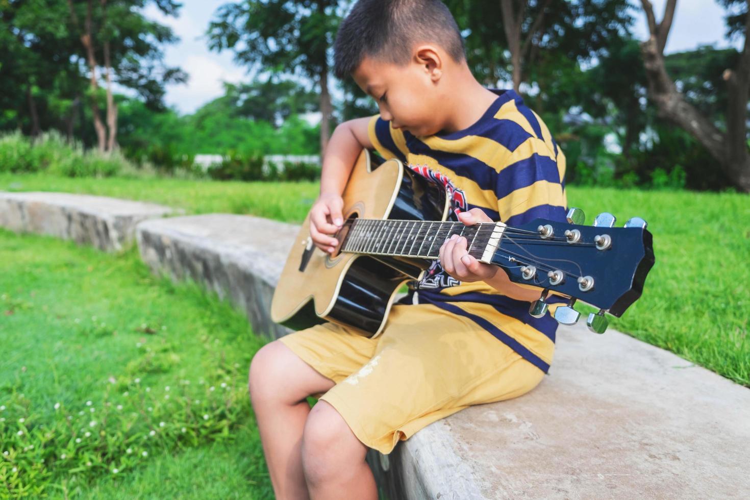 Junge spielt eine Gitarre in einem Park foto