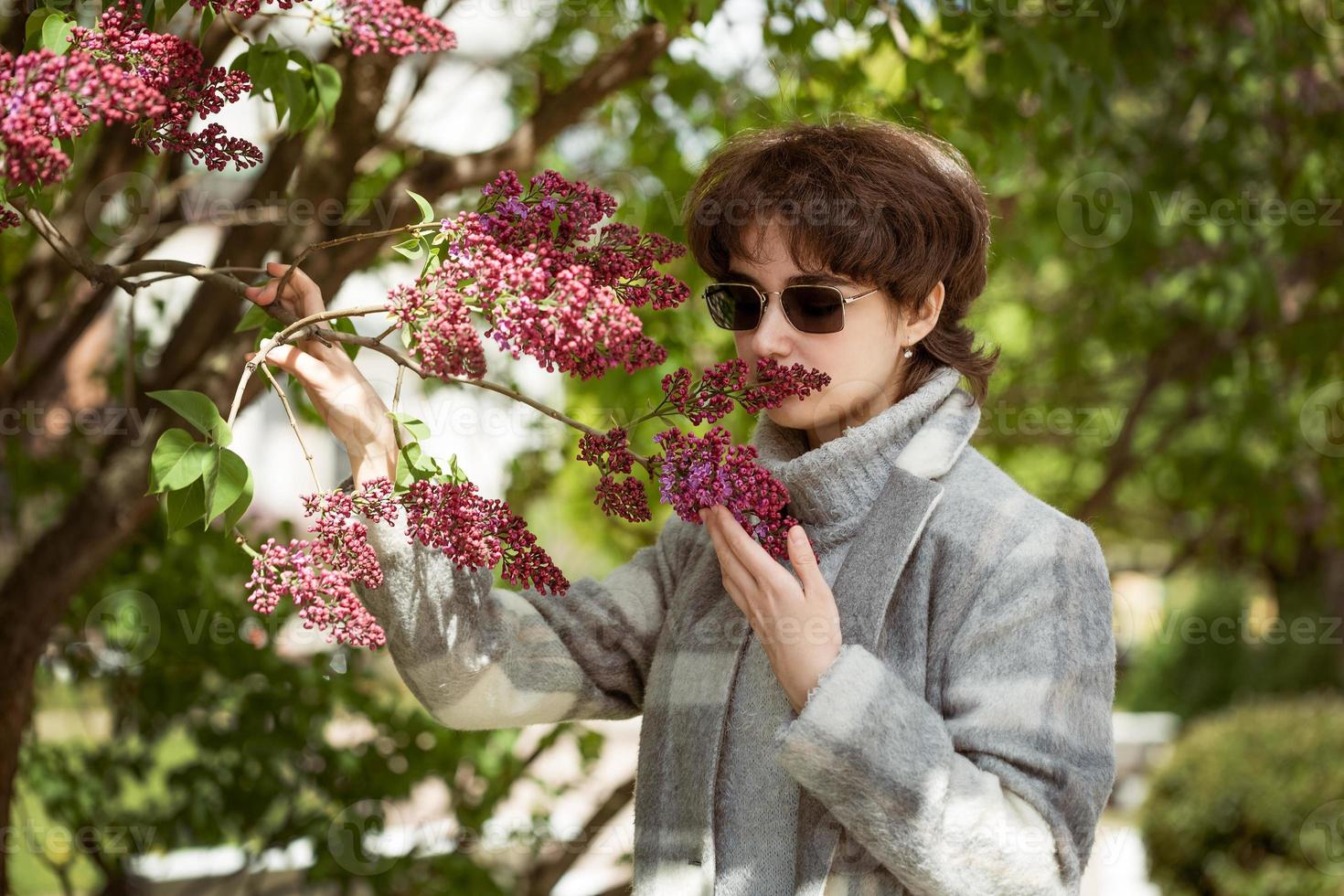 Porträt von ein jung Frau im Sonnenbrille in der Nähe von ein lila Busch foto