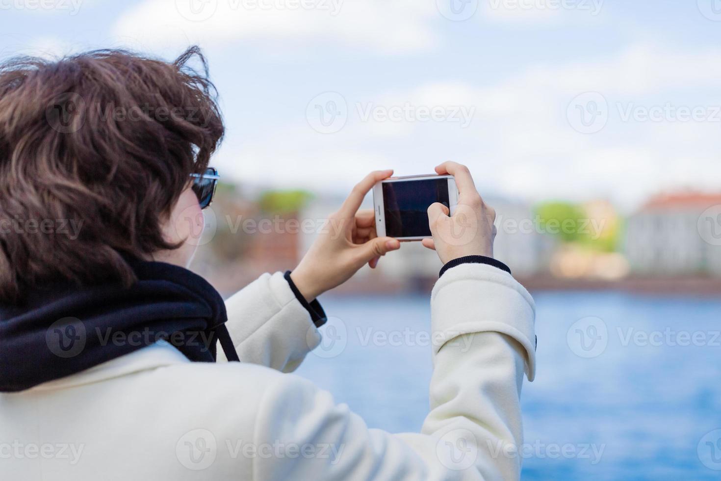 jung Frau auf Ferien mit Handy, Mobiltelefon Telefon zu nehmen Bilder Fluss und Stadt foto