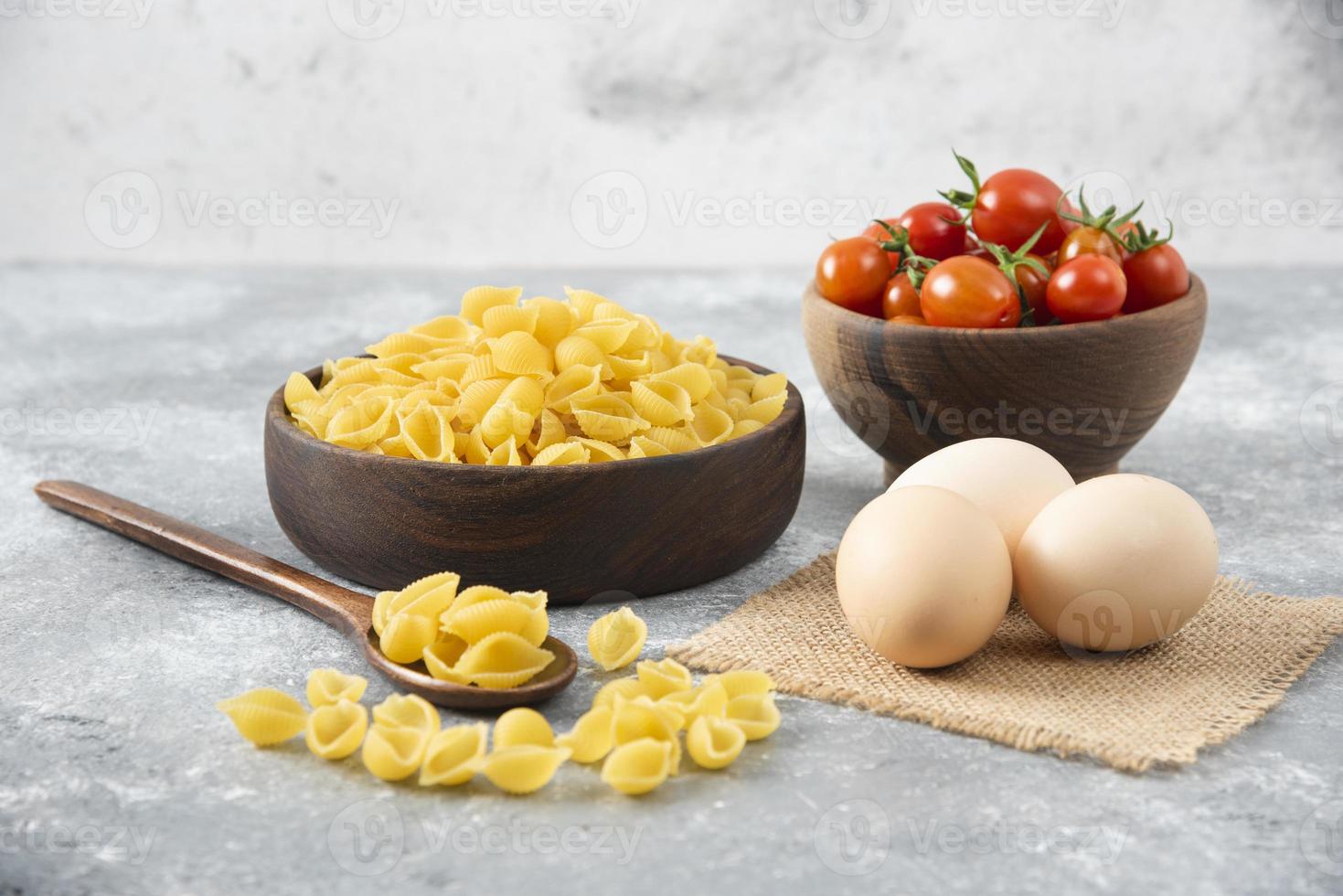 ungekochte schalenförmige Nudeln mit rohen Hühnereiern auf einem Steintisch foto