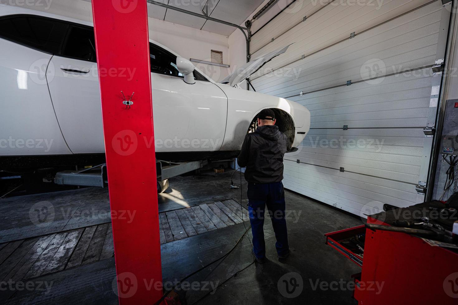 Mechaniker in Service-Reparaturstation, der mit Muscle-Car arbeitet, zerlegt ein Rad auf der Hebebühne. foto