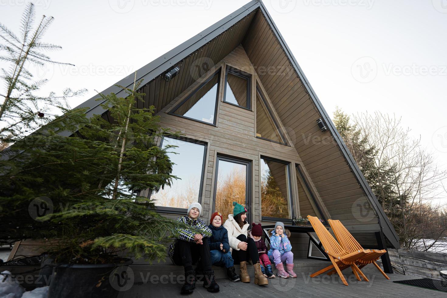 Mutter mit vier Kinder sitzen auf Terrasse aus Gitter winzig Haus im das Berge. foto