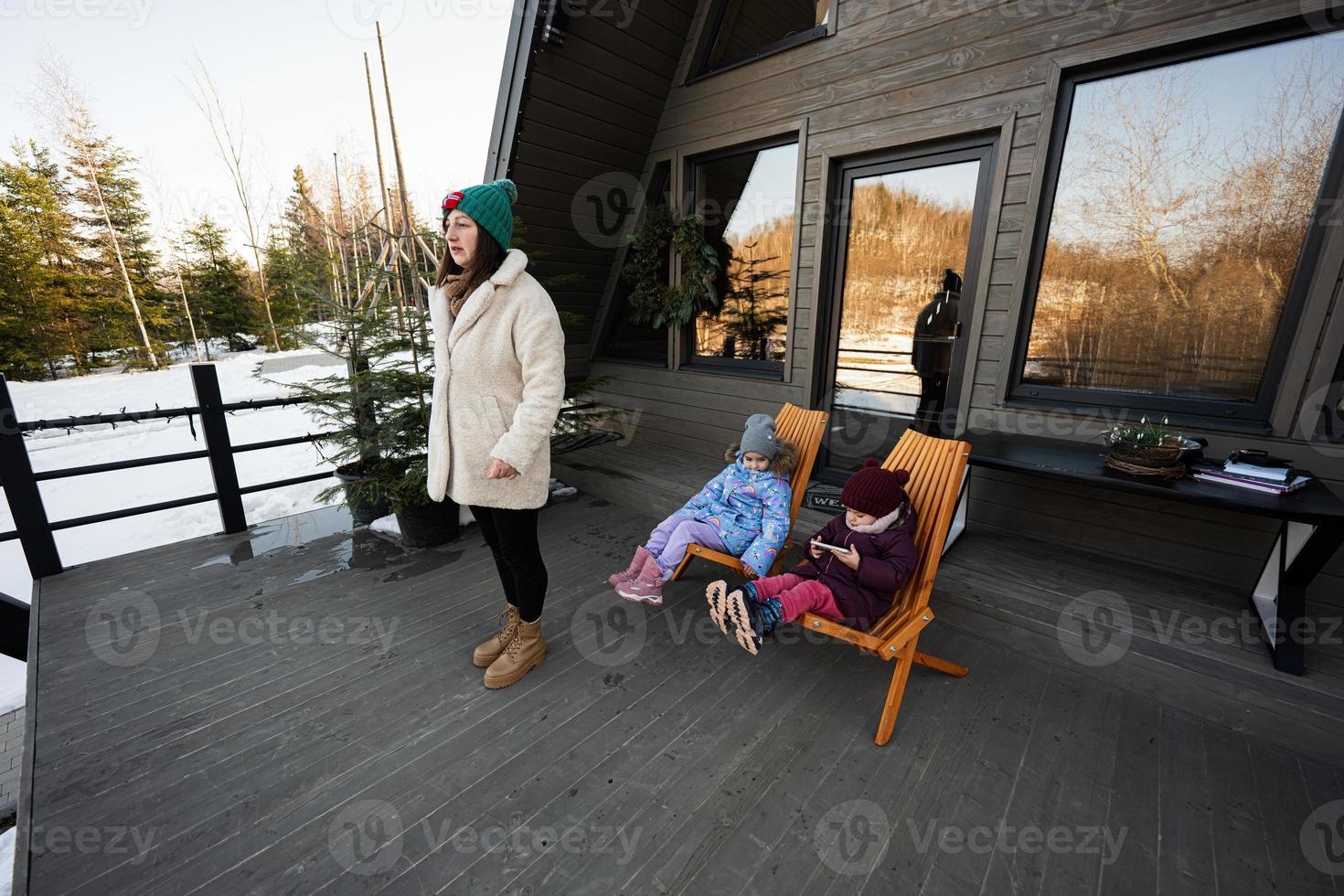 Mutter mit zwei Töchter auf Terrasse aus Gitter winzig Haus im das Berge. foto