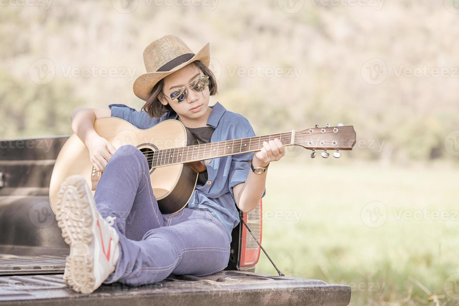 Frau trägt Hut und spielt Gitarre auf Pickup-Truck foto