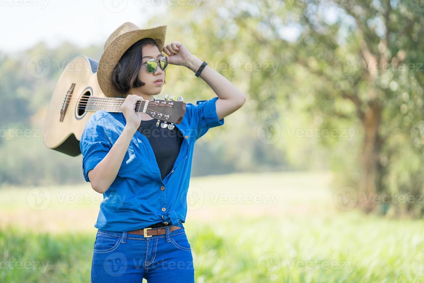 Frau trägt Hut und trägt ihre Gitarre auf der Wiese foto