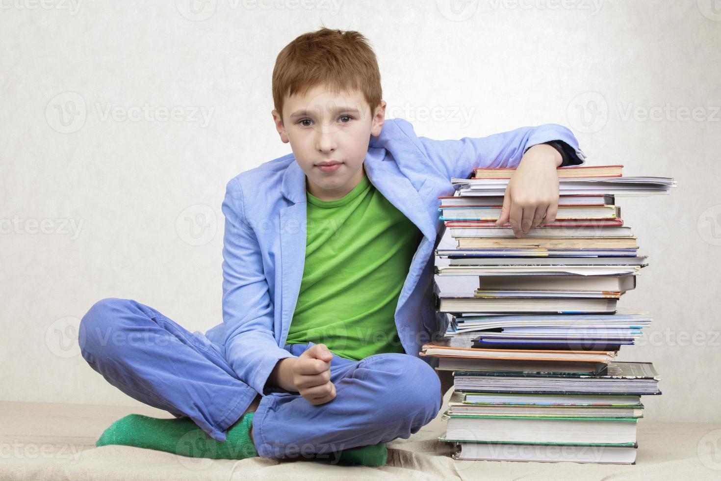 ein Mitte Schule Junge beugte sich vor auf ein Stapel von Bücher. foto